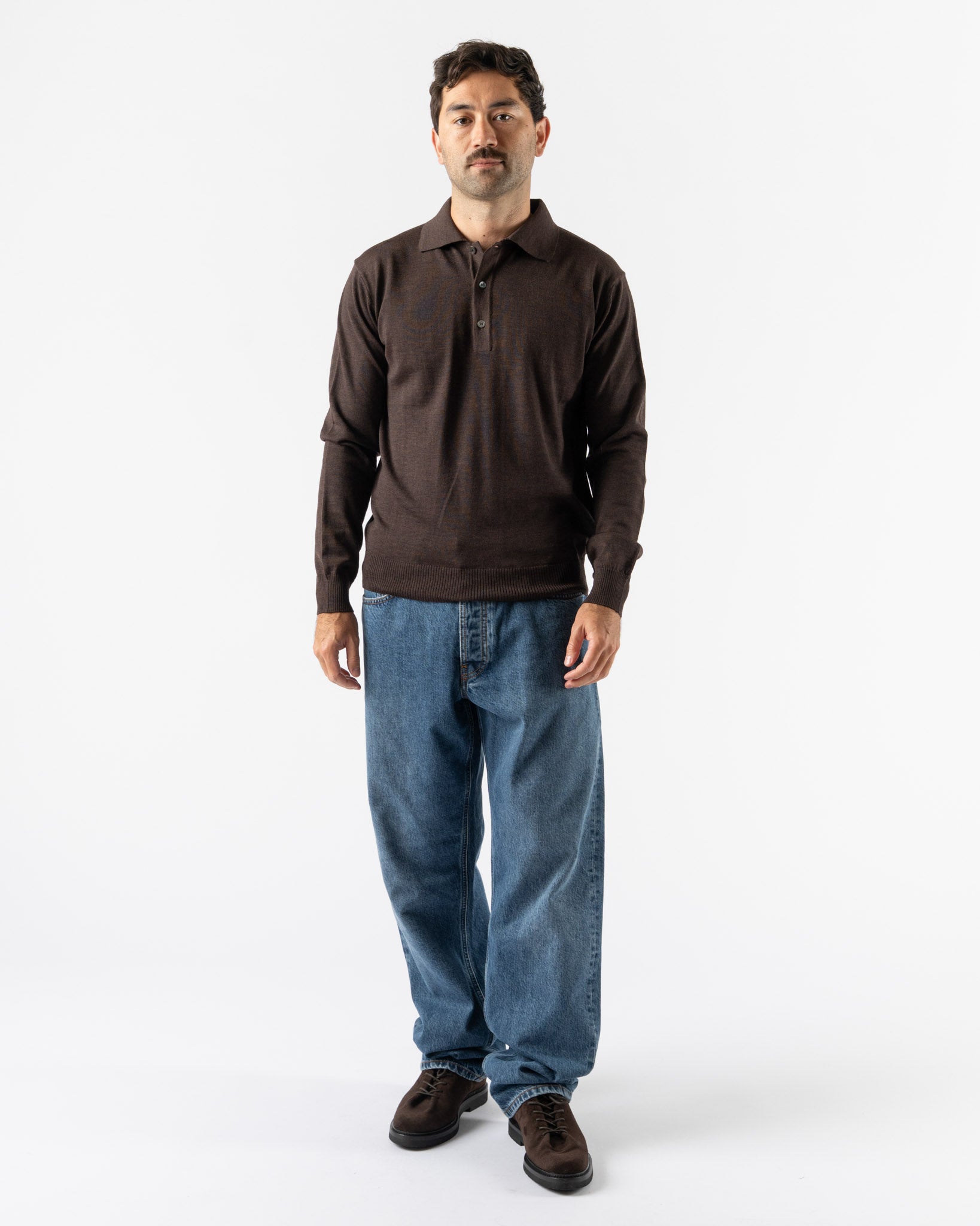 Man wearing a brown long-sleeve shirt and blue jeans on a white background