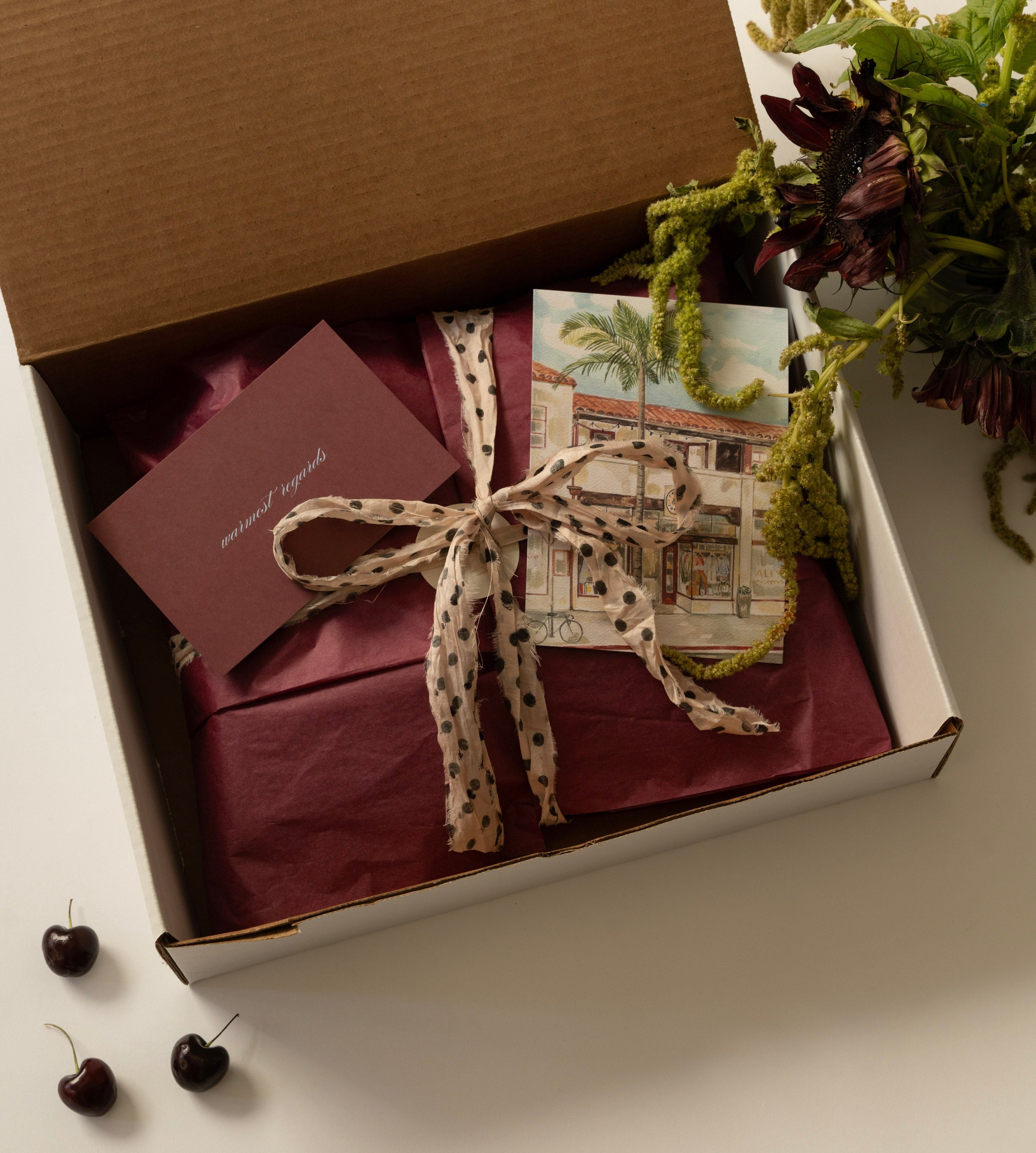 Gift box with a bow, cards, and a small plant on a light surface.