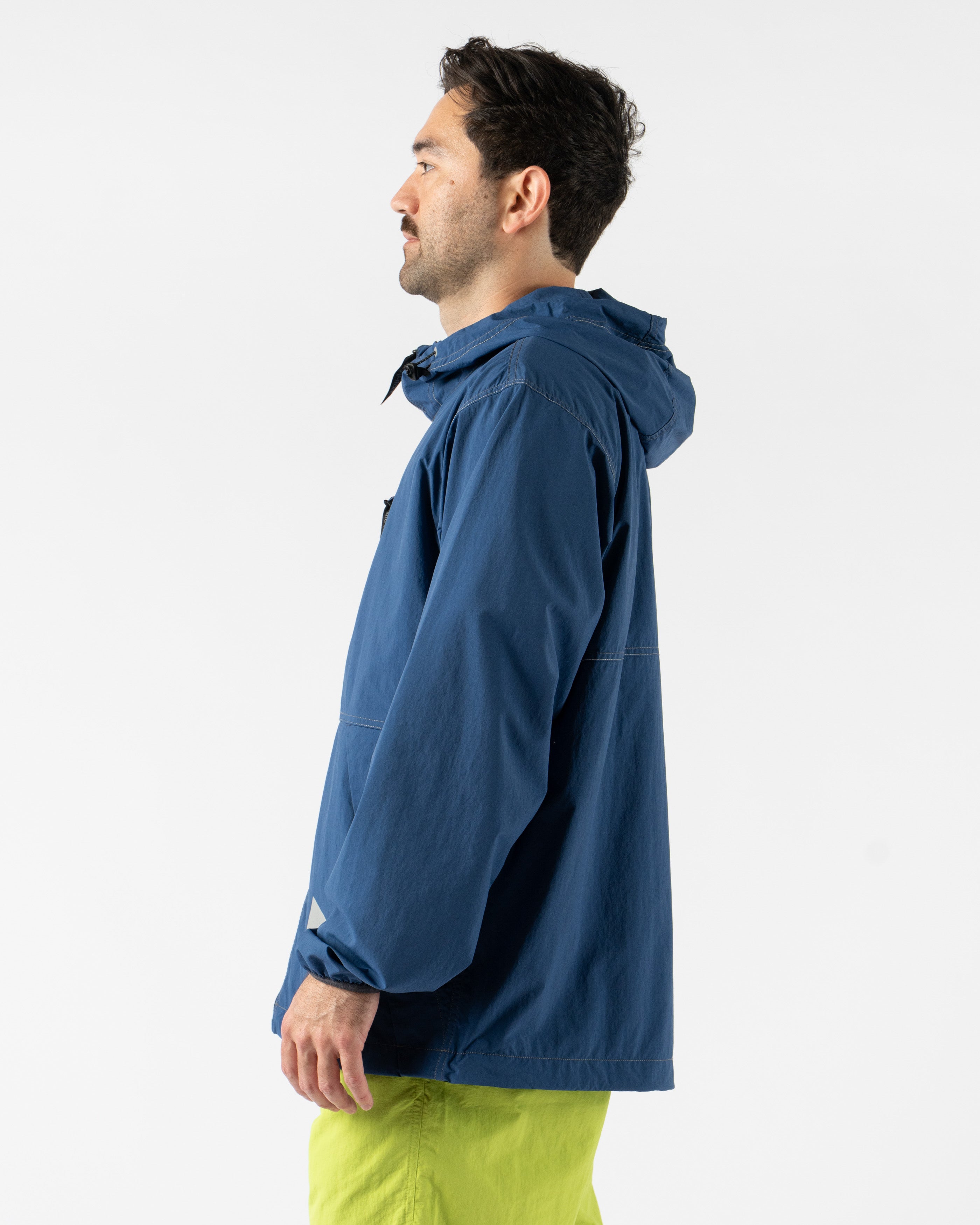 Gramicci x and wander Brushed Nylon Jacket in Blue shown in various angles, featuring lightweight water-repellent nylon, reflective stitching, zippered pockets, and an oversized fit designed for both outdoor performance and urban style. Highlighting articulated sleeves, stand collar, and technical construction in a sleek matte blue finish.