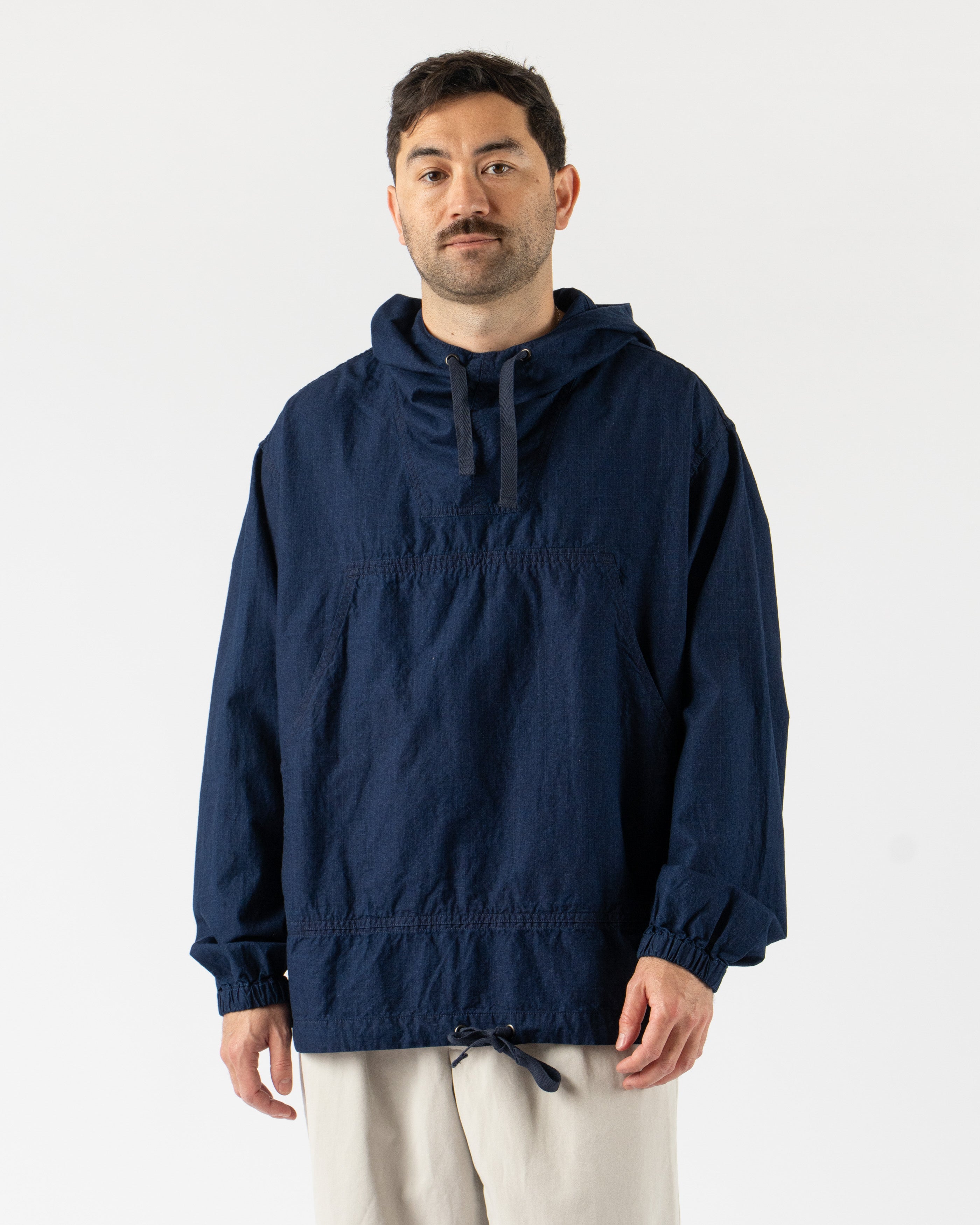  Beams Plus MIL Smock in Indigo Ripstop – military-inspired pullover smock crafted from durable indigo-dyed ripstop fabric, featuring a half-zip front, adjustable hood, large utility pockets, and a relaxed fit for functional everyday wear.