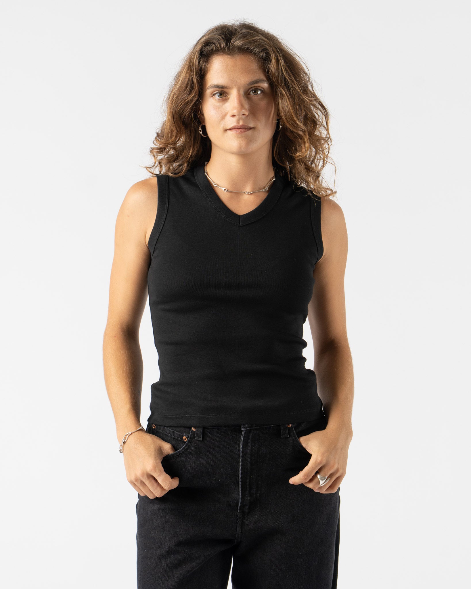 Person wearing a black sleeveless top and dark jeans on a white background