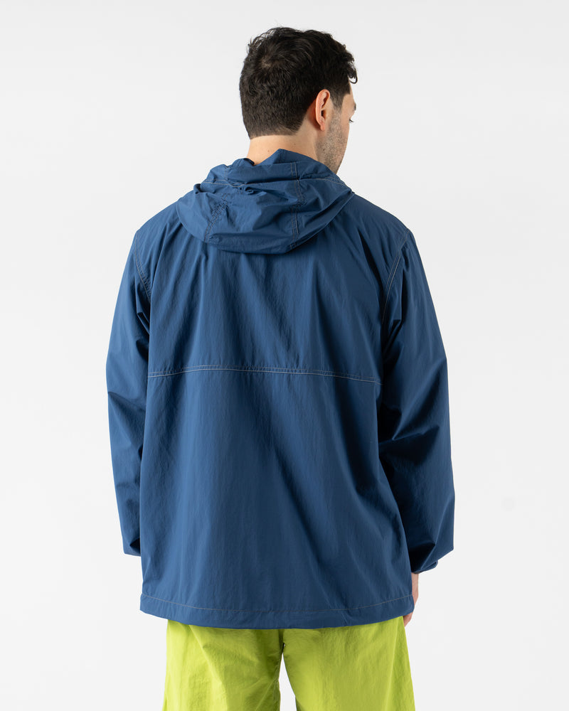 Gramicci x and wander Brushed Nylon Jacket in Blue shown in various angles, featuring lightweight water-repellent nylon, reflective stitching, zippered pockets, and an oversized fit designed for both outdoor performance and urban style. Highlighting articulated sleeves, stand collar, and technical construction in a sleek matte blue finish.