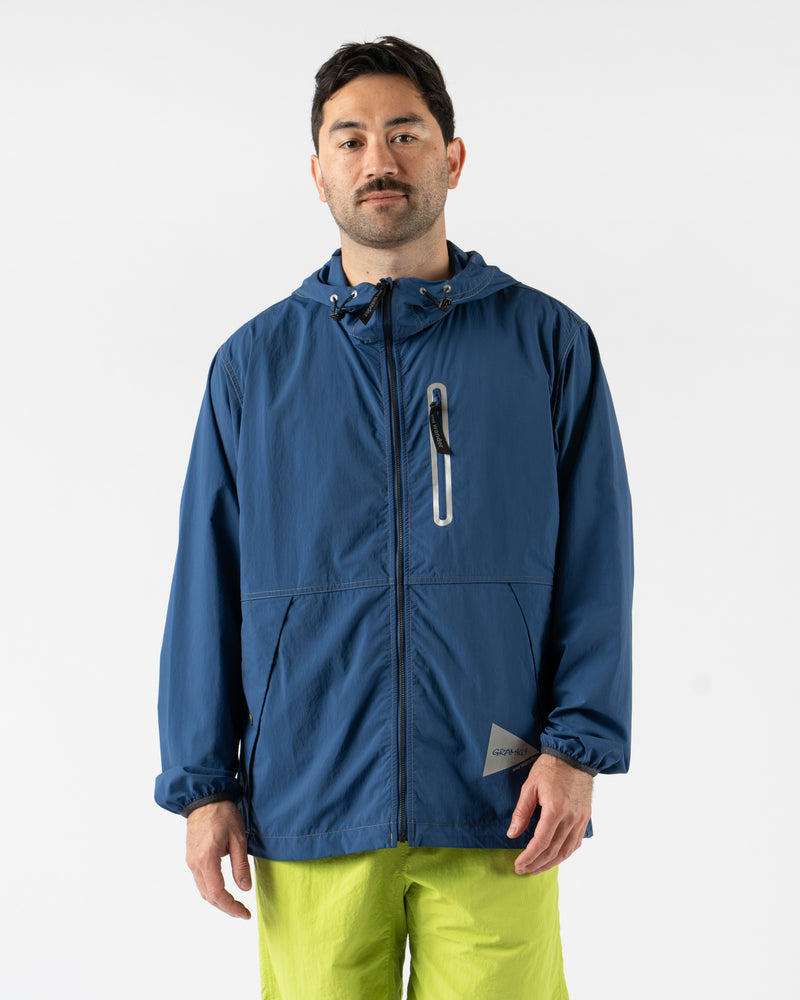 Gramicci x and wander Brushed Nylon Jacket in Blue shown in various angles, featuring lightweight water-repellent nylon, reflective stitching, zippered pockets, and an oversized fit designed for both outdoor performance and urban style. Highlighting articulated sleeves, stand collar, and technical construction in a sleek matte blue finish.