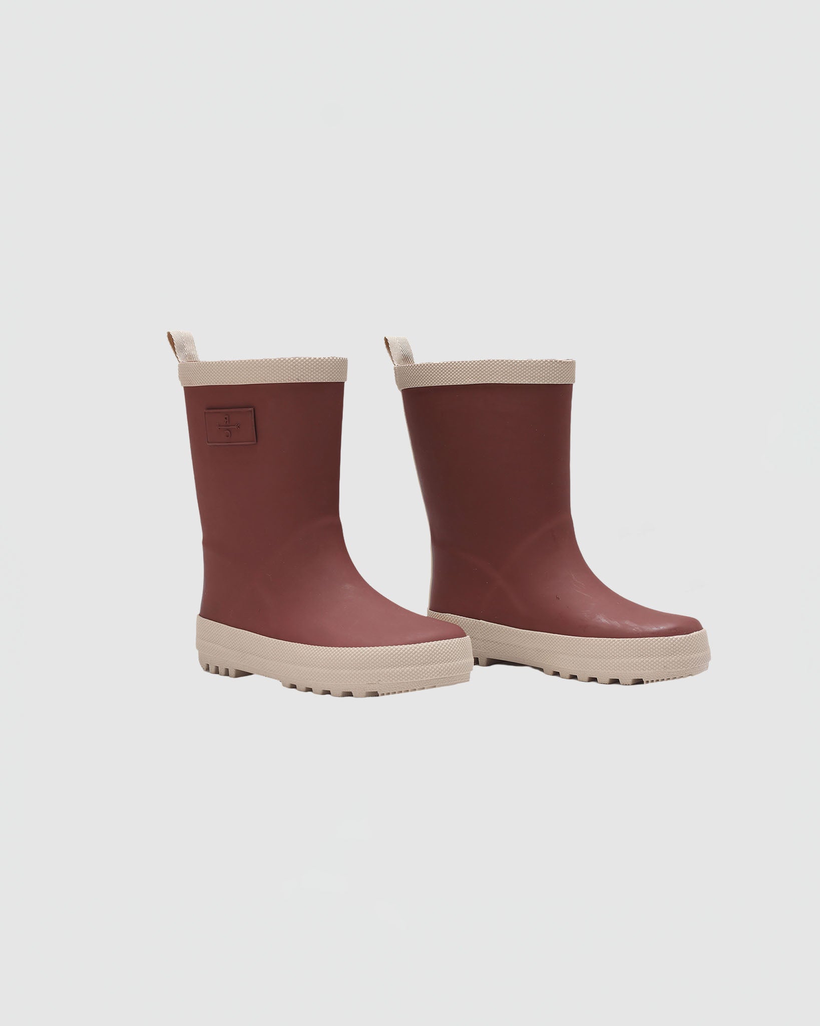 Pair of maroon rain boots with beige accents on a light gray background