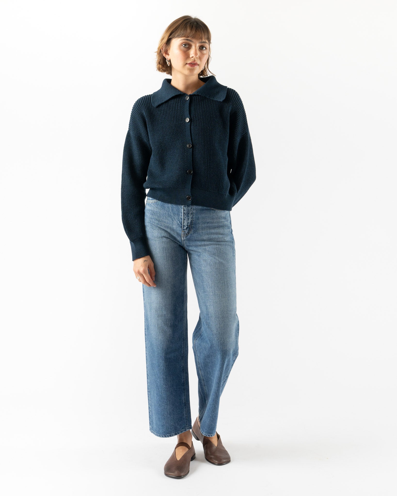 Person wearing a dark blue cardigan and light blue jeans on a white background