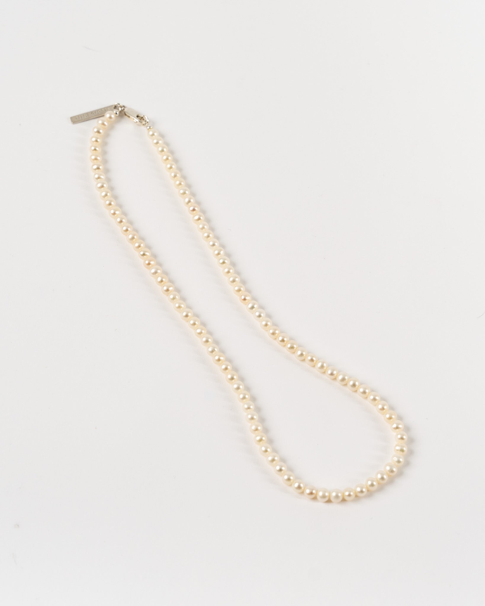A single-strand natural freshwater pearl necklace with a silver clasp, laid out on a white surface.